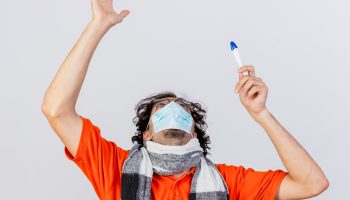 young caucasian ill man wearing glasses scarf and mask holding thermometer looking up raising up hand isolated on white background